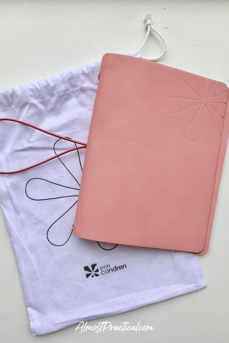 The Erin Condren On the Go Folio cover in mauve laying on top of the white drawstring cloth bag emblazoned with the Erin Condren logo that it came in.