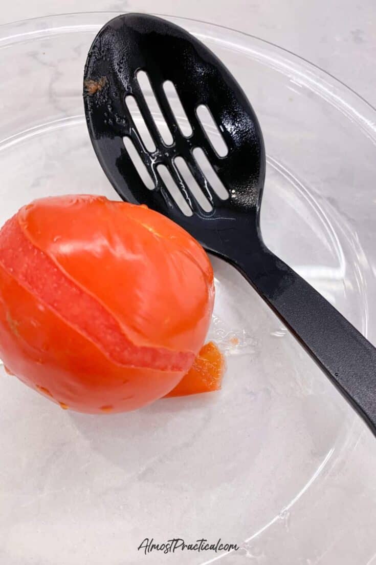 one blanched tomato in a glass pie plate next to a slotted spoon.