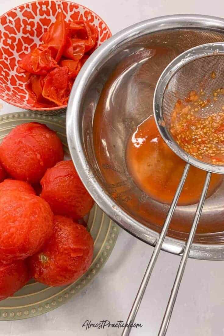 a stainless steel fine mesh strainer over a stainless steel mixing bowl that is being used to strain tomato seeds.