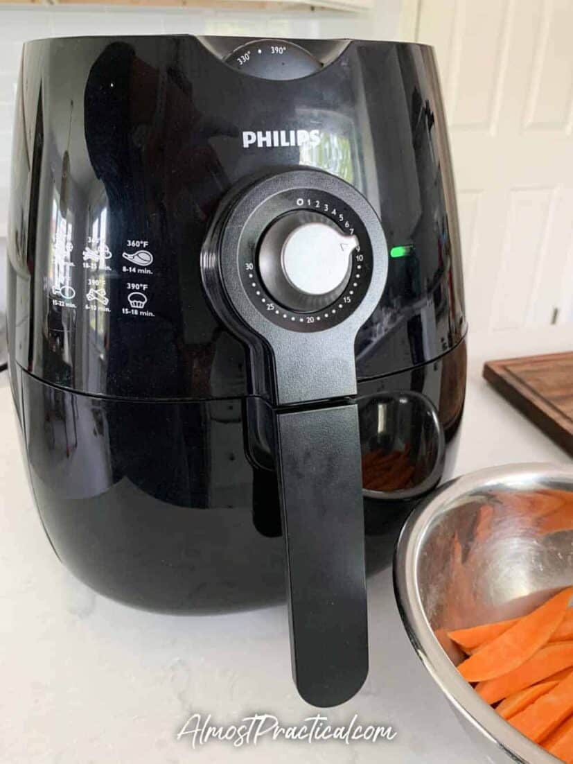 Air fryer next to a mixing bowl of raw sweet potato fries.
