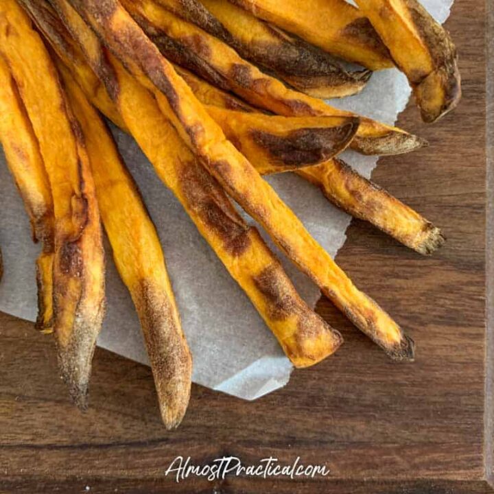 cooked sweet potato fries on a piece of parchment paper on a walnut cutting board