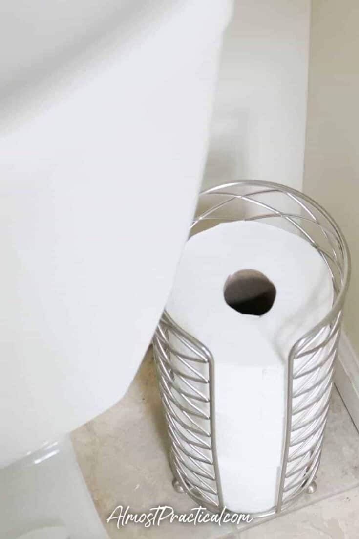 decorative silver toilet paper storage tower in corner of bathroom behind toilet