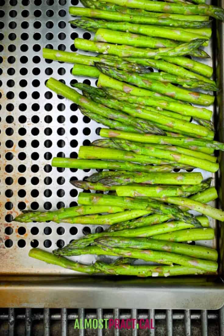 Asparagus in grill topper pan with holes cooking on the grill.