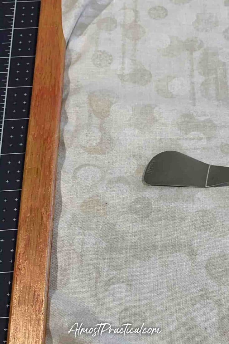 Cricut spatula used to push fabric underneath bulletin board frame.