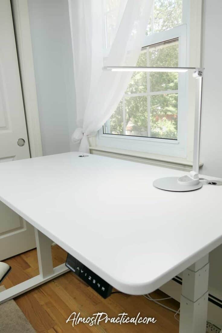 White standing desk with desk lamp on top.