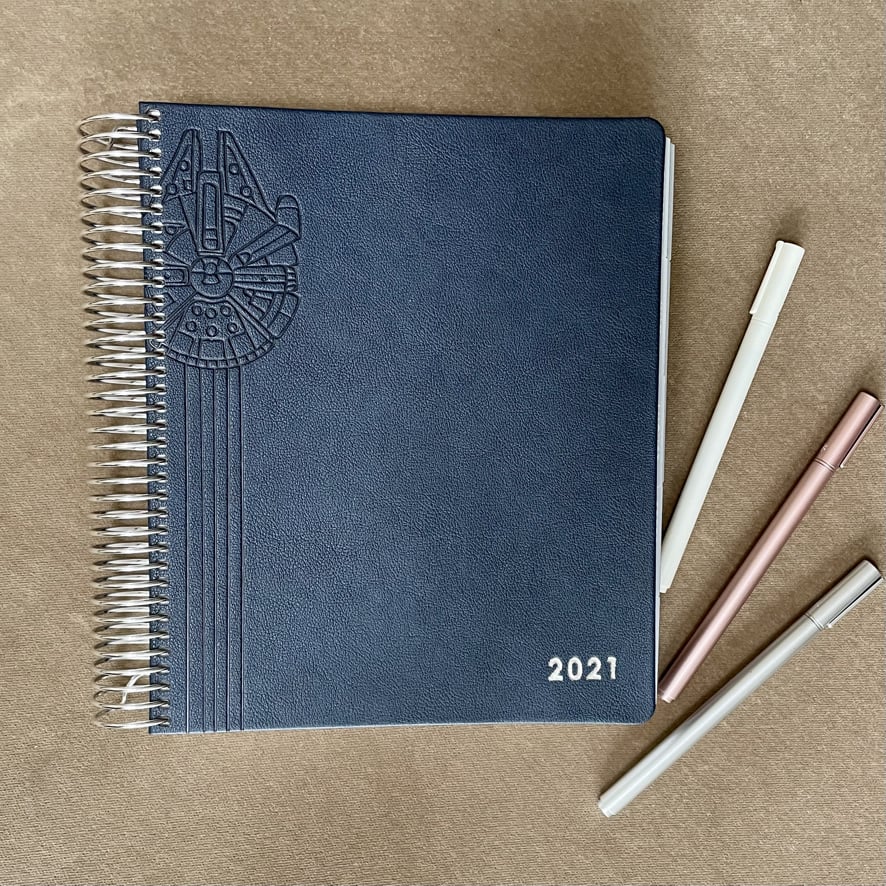the Erin Condren LifePlanner with a navy vegan leather cover that is embossed with the Star Wars Millenium Falcon