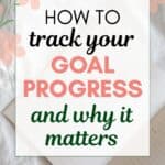 words "how to track your goal progress and why it matters" superimposed on an image of an open planner on a white fabric background