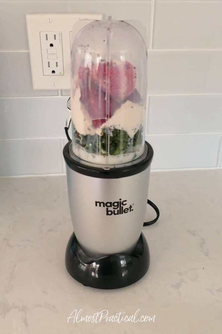 Magic Bullet blender with cup filled with kale, yogurt, and frozen strawberries ready to blend.