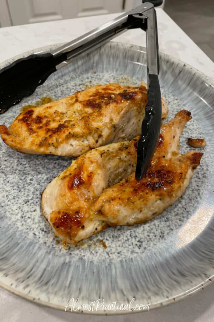 pan roasted chicken breast on a plate with tongs.