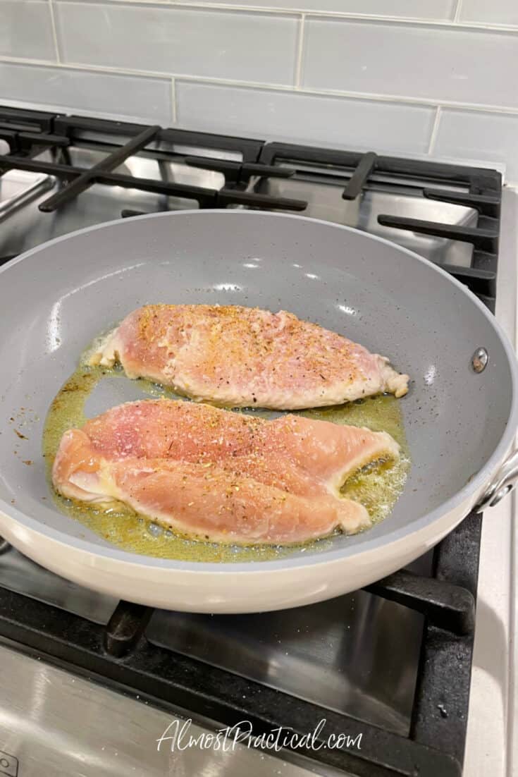 chicken breasts cooking in a fry pan on stove