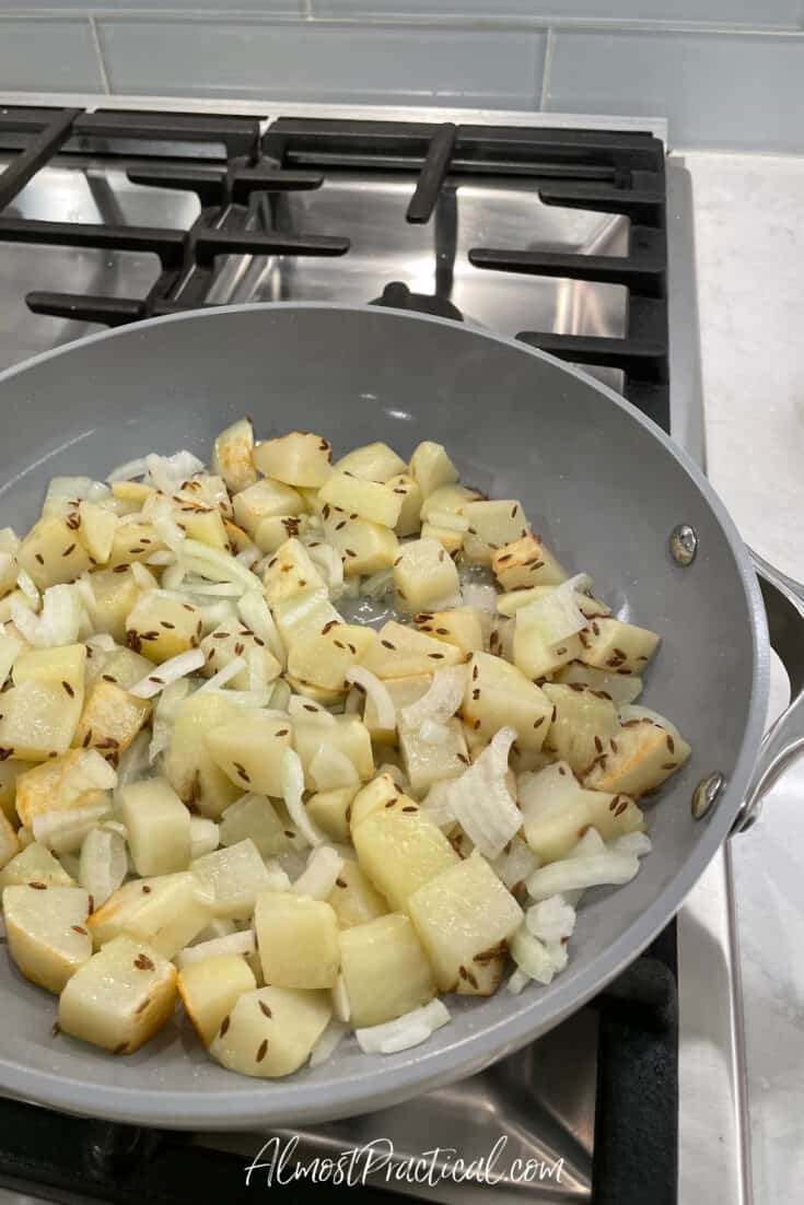 diced potatoes, sliced onions, and cumin seeds cooking in skillet on stove