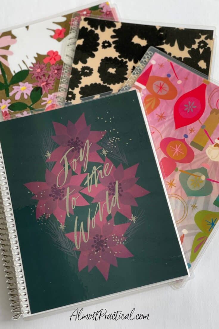 a spiran bound notebook with a cover that says Joy to the World on top of maroon poinsettias and black background. Plus 3 other covers in various designs.