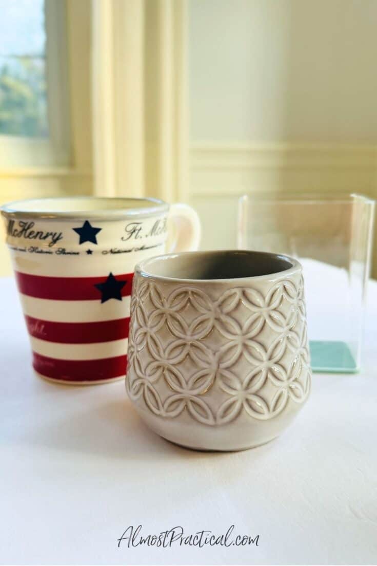 A red white and blue mug, a small grayish ceramic cup, and a rectangular acrylic pen cup.