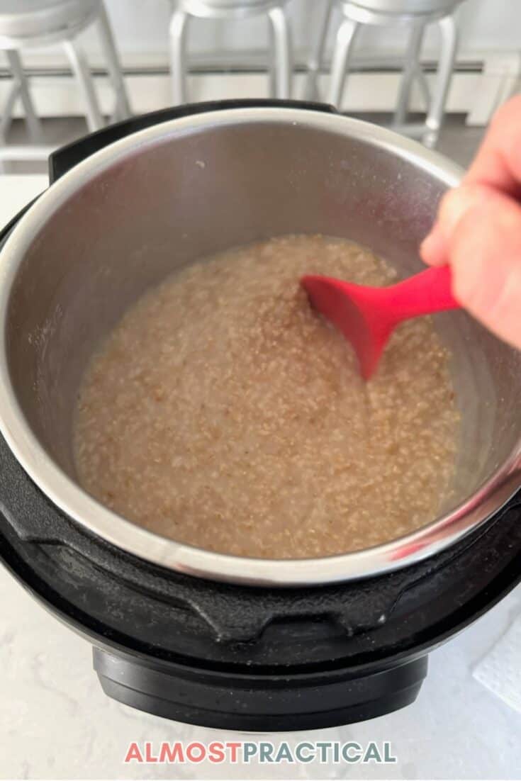 stirring the cooked steel cut oatmeal in the instant pot with a red silicone spoon