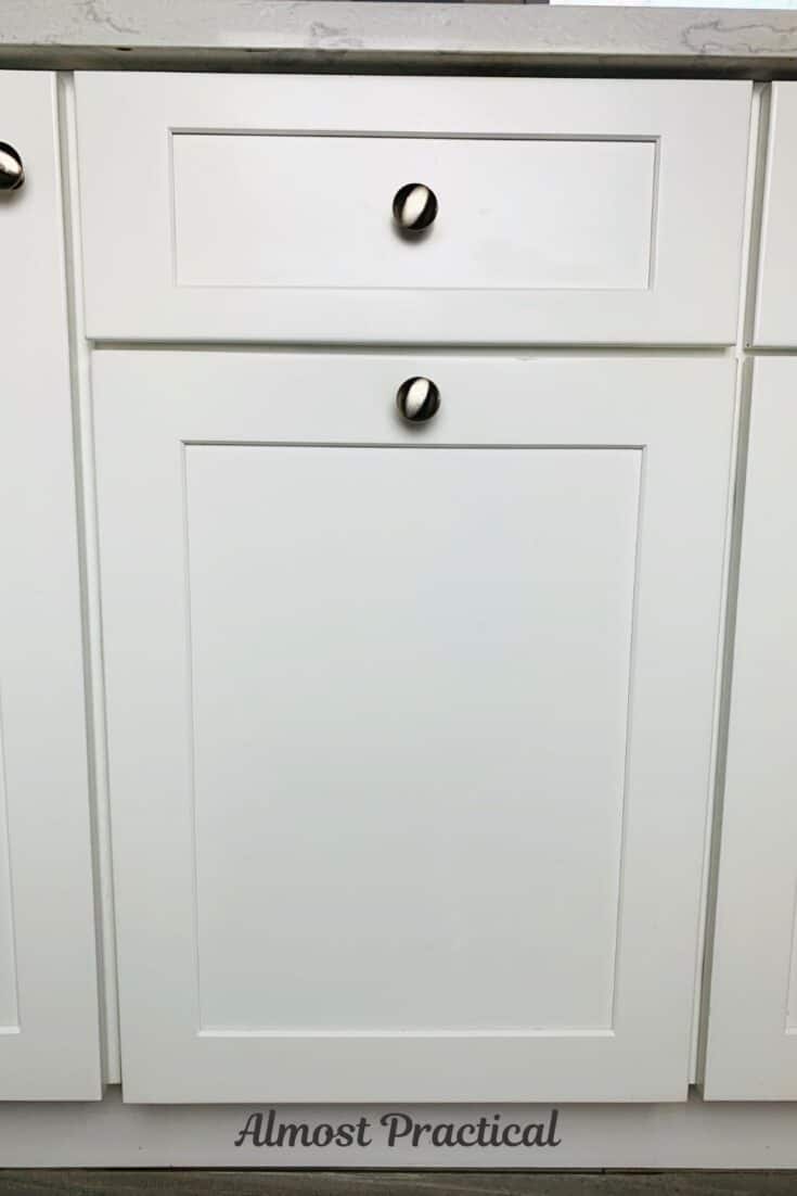 white kitchen pull out trash cabinet with a silver knob