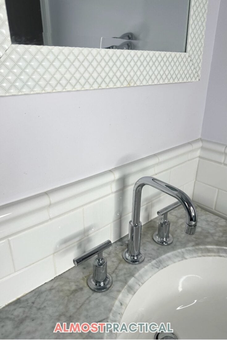bathroom faucet on marble vanity top with white subway tile backsplash and white framed mirror above