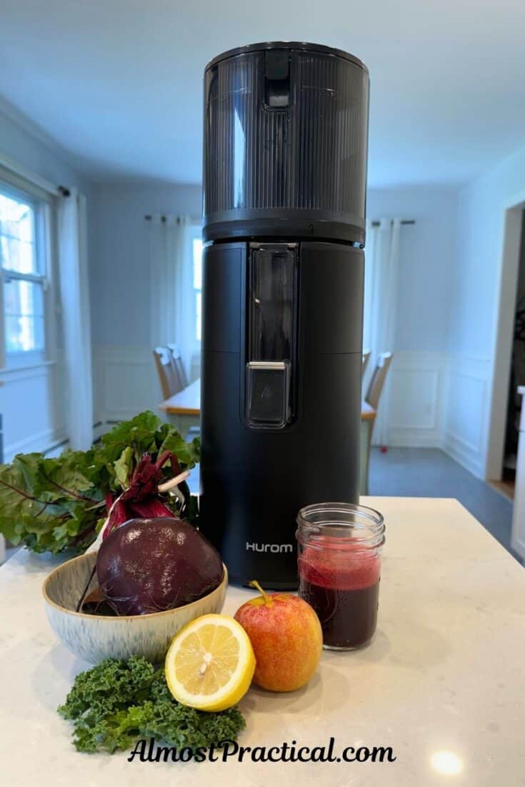 The Hurom H400 juicer surrounded by a variety of fruits and vegetables and a glass of beet juice.