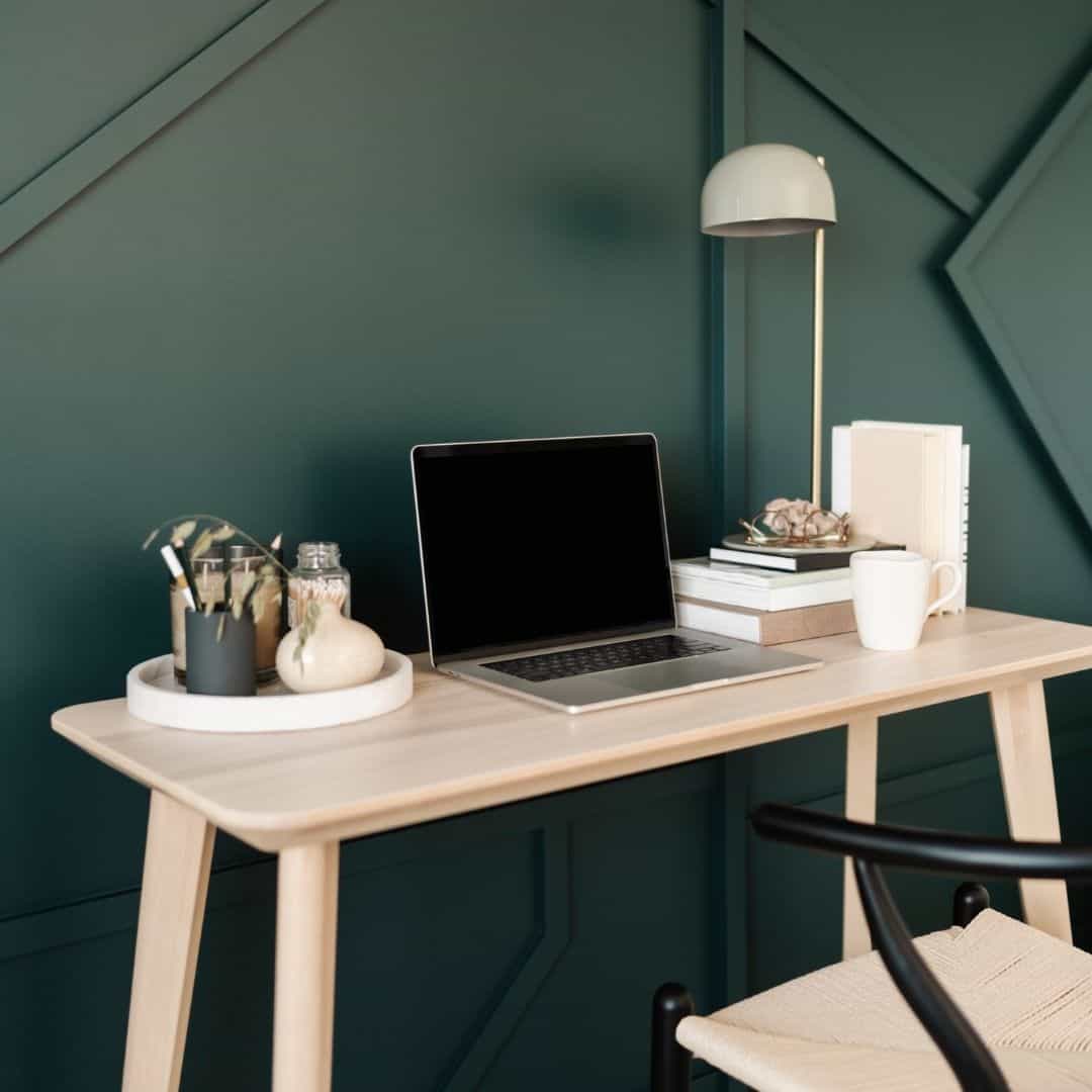photo of a home office desk with an open laptop and green wall behind it