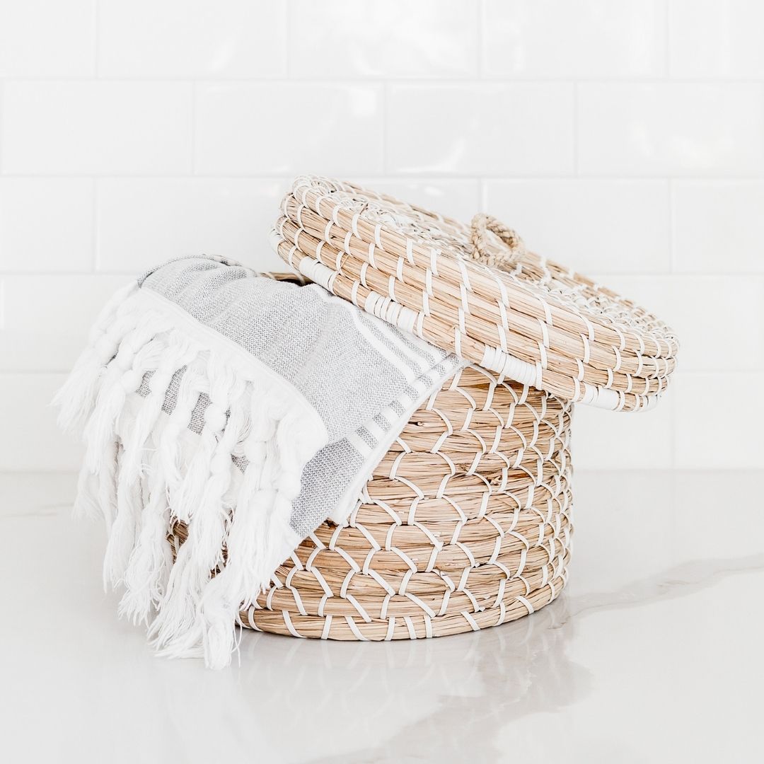 photo of a wicker basket with lid slightly ajar and a gray turkish towel hanging out of it