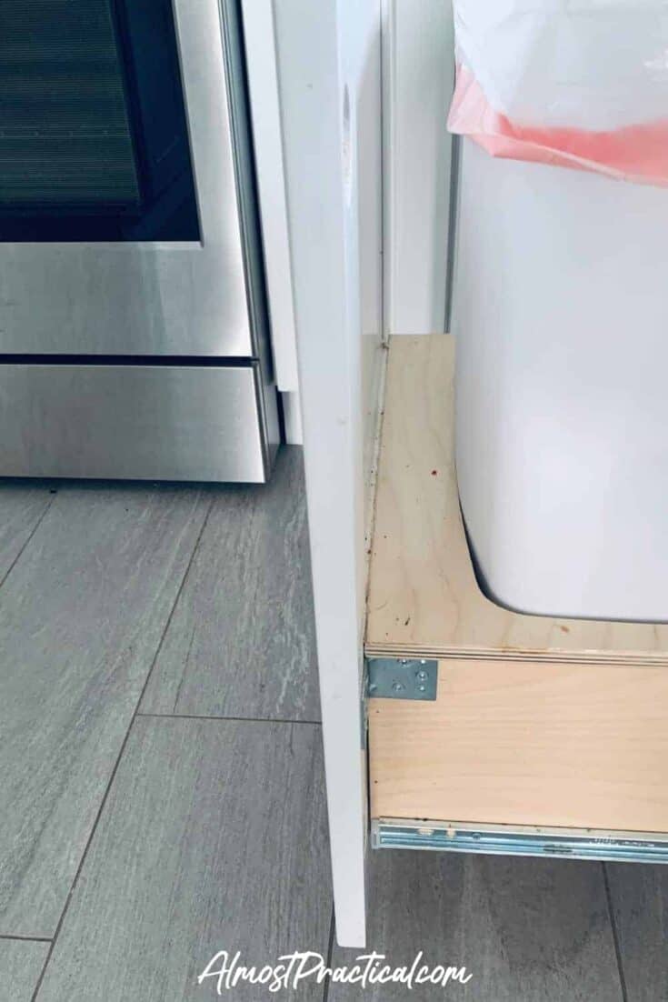 Pull out trash can cabinet with crumbs around the base.